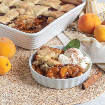 Vegan peach cobbler served up in a white dish with a scoop of ice cream.