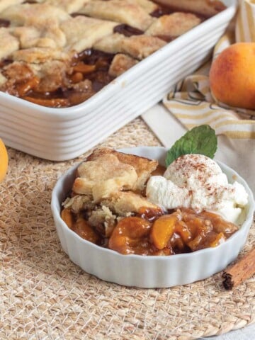 Vegan peach cobbler served up in a white dish with a scoop of ice cream.