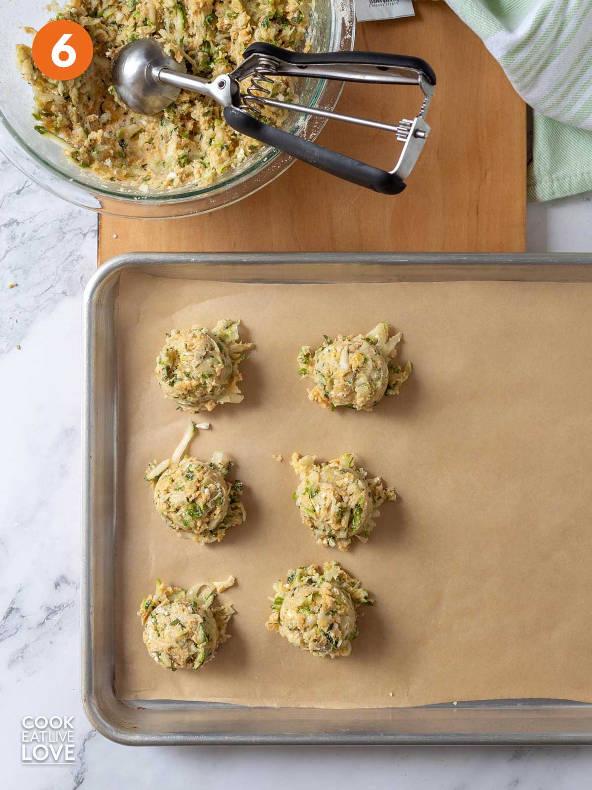 Balls of zucchini fritters scooped onto a baking tray.