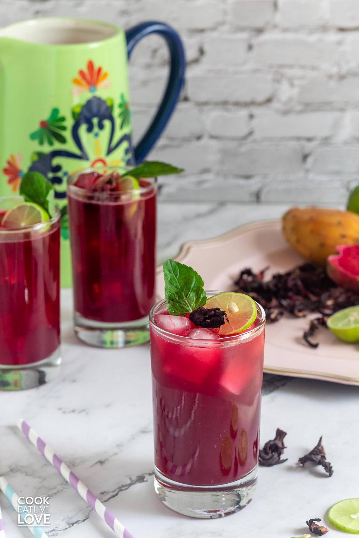 Glasses of fresh prickly pear water on the table with a plate of whole and halved fruits.