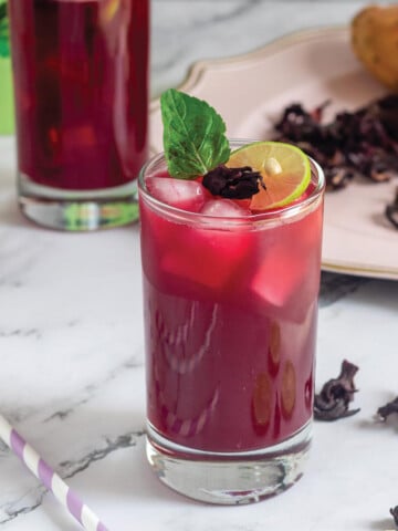 A glass of prickly pear hibiscus agua fresca on the table with a straw to the side.