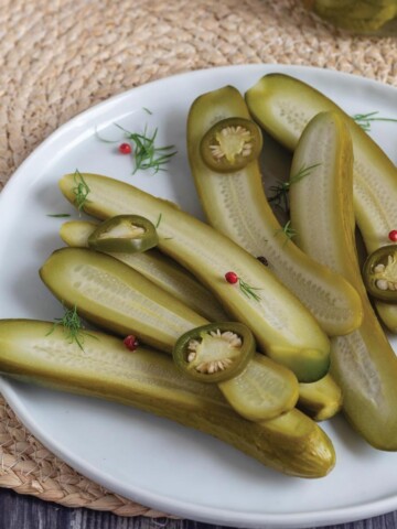Refrigerator dill pickle halves on a plate with slices of jalapenos.