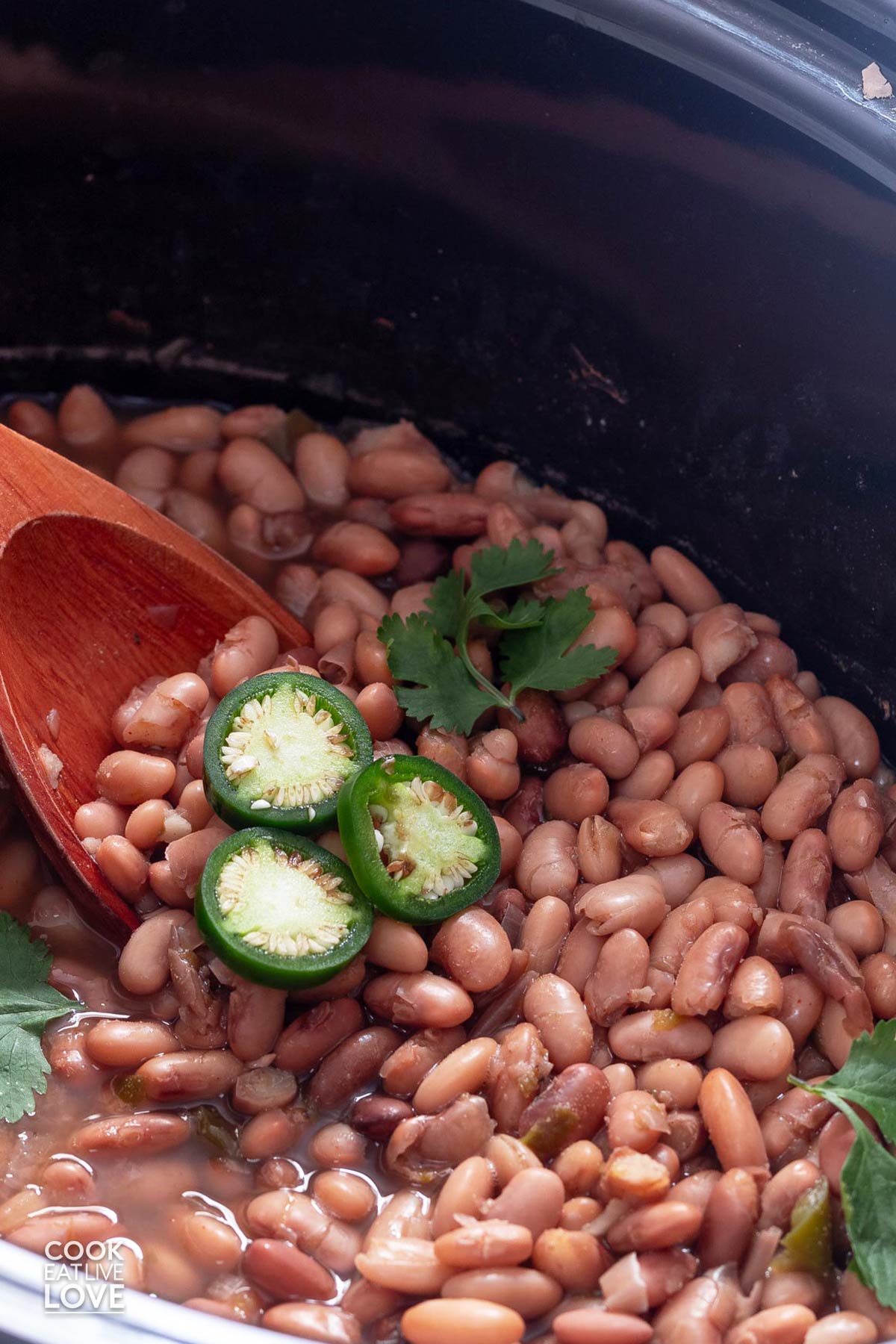 Pinto beans in the crockpot with a wooden spoon and cilantro and jalapeno.