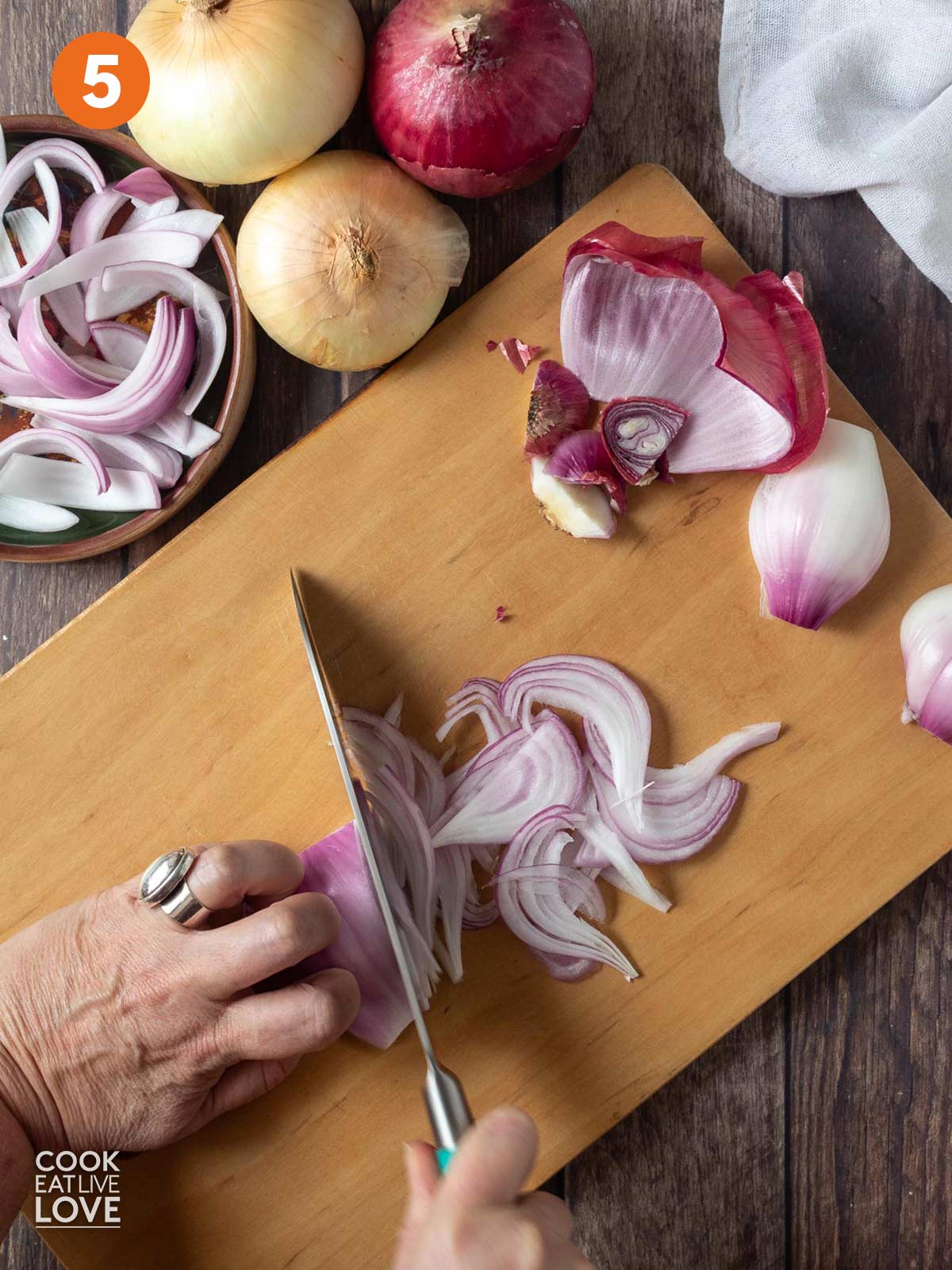 A hand holding the onion and the other hand cutting with a knife into slices.