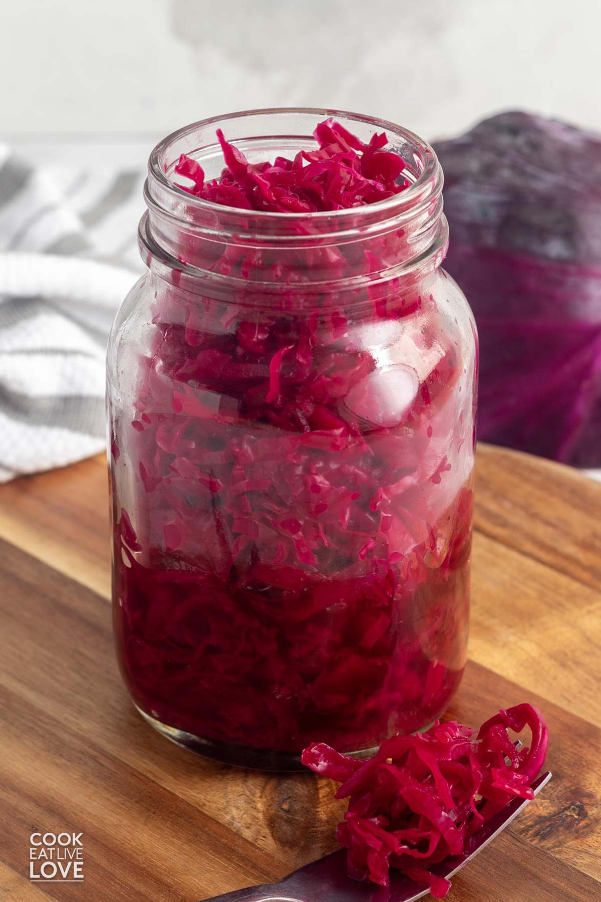 A jar of red sauerkraut on the table with a forkful next to the jar.