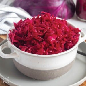 Red cabbage sauerkraut in a bowl on a plate in front of purple cabbage.
