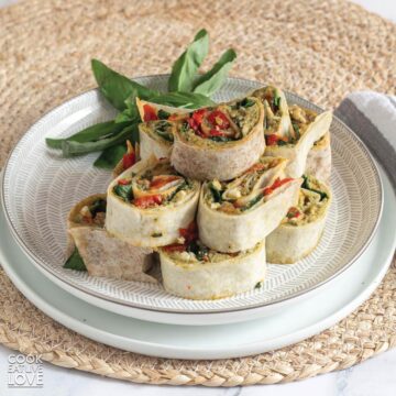 Vegan pinwheels on a small white plate on the table and garnished with fresh basil.