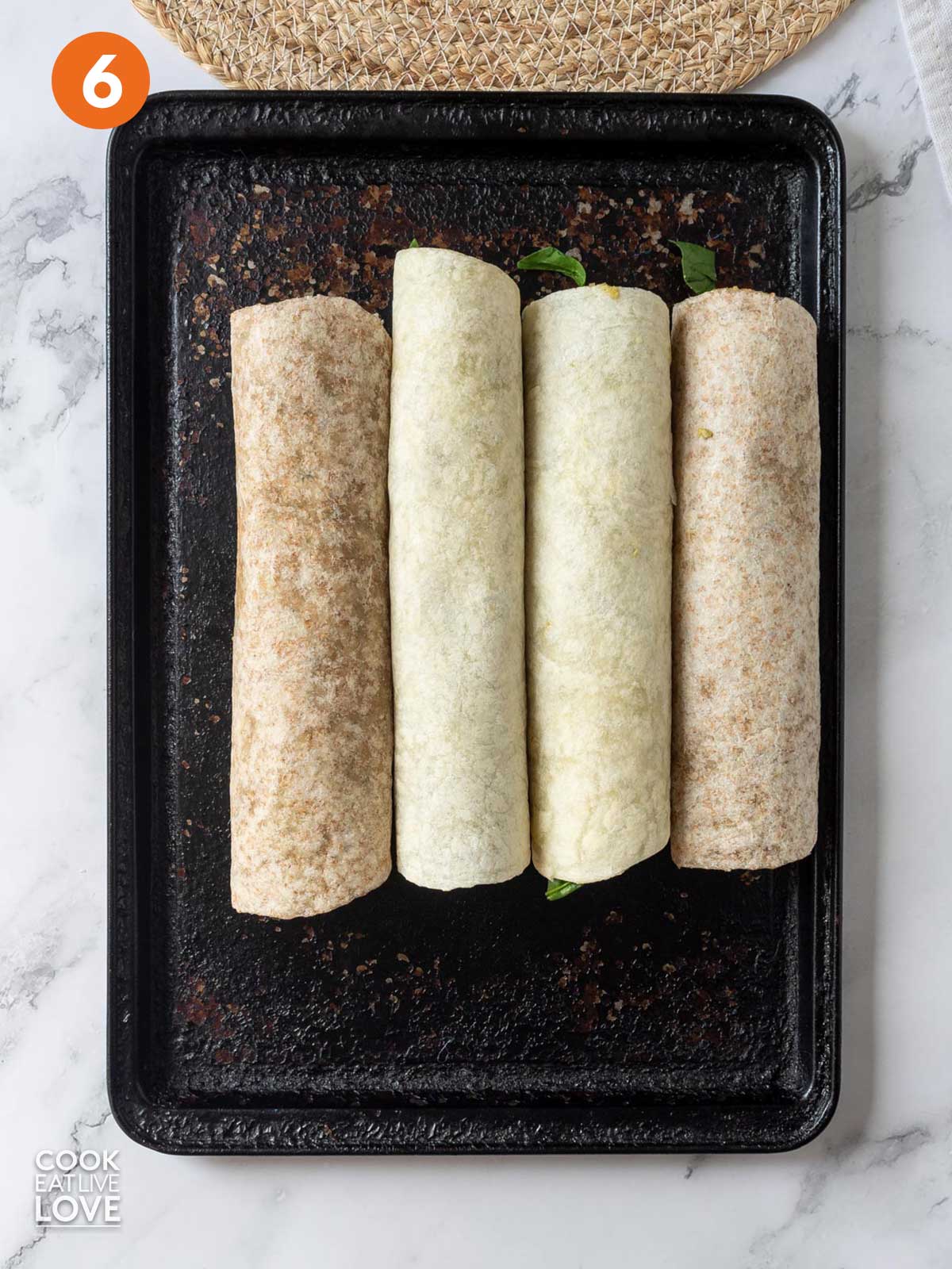 Rolled up flour tortillas are on a baking tray.