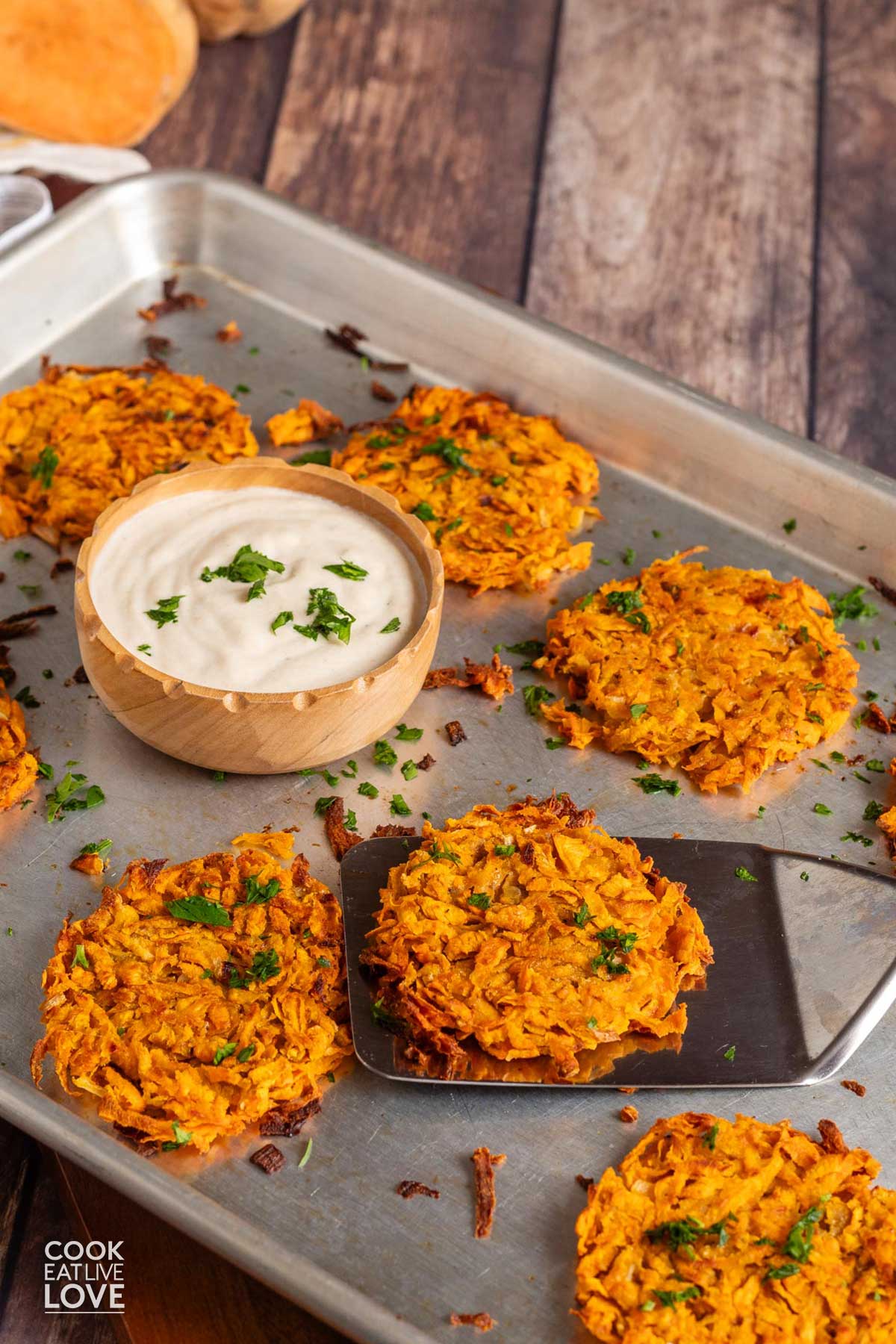 Sweet potato hashbrowns on a baking tray with a small bowl of sauce.