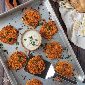 Sweet potato hashbrowns on a baking tray with a spatula underneath one and a bowl of sauce in the middle.