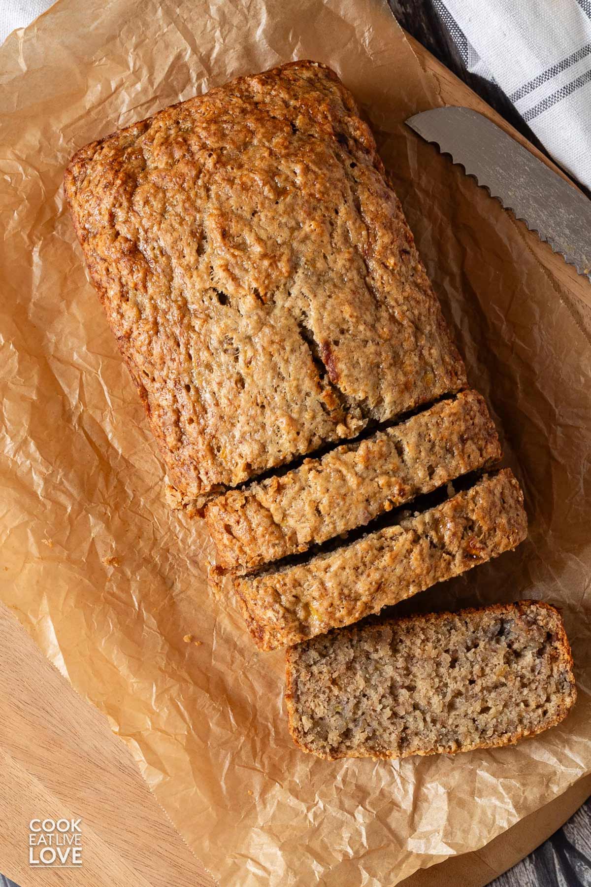 A loaf of no butter banana bread on the table with three slices cut and one laying over on its side.