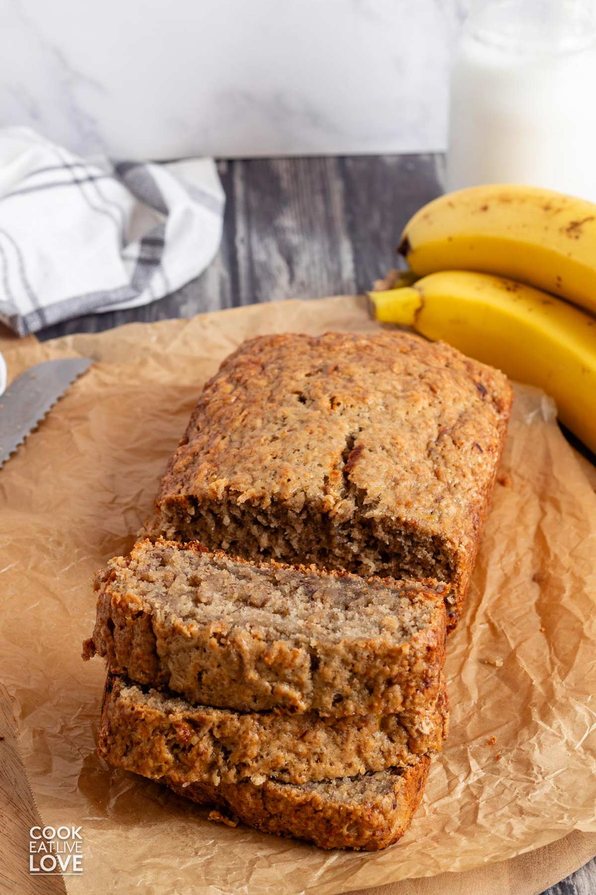 A loaf of no butter banana bread on the table with a few slices in front.