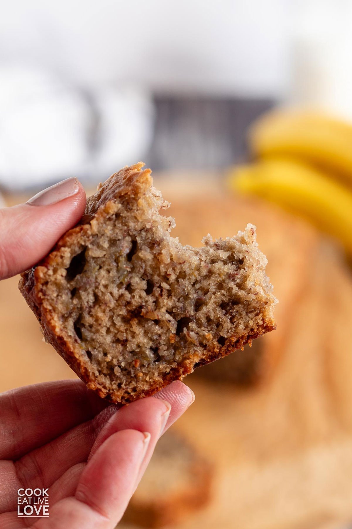 A hand holding up a piece of banana bread no butter with a bite missing.