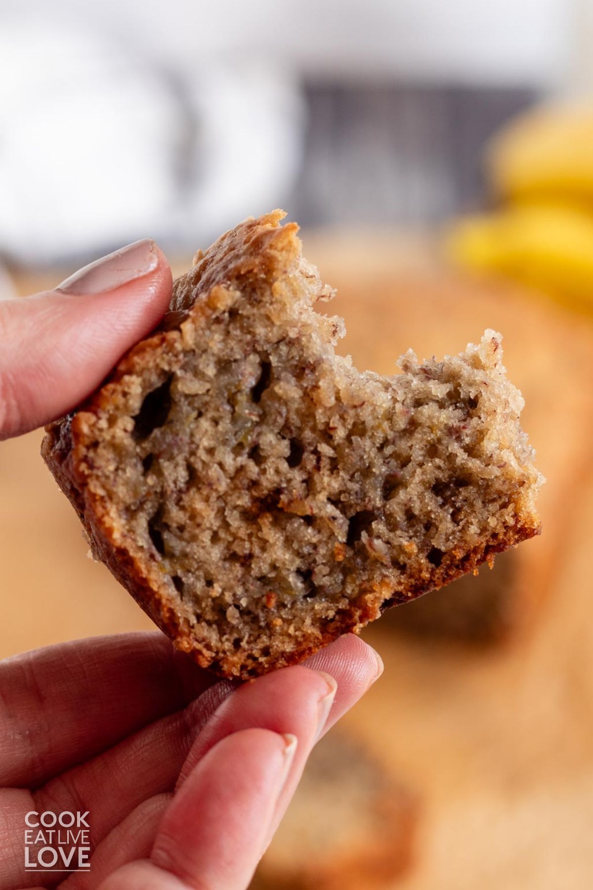 A hand holding up half a piece of dairy-free banana bread made with oil and a bite taken. 