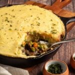 Mushroom shepherd's pie served up in a skillet on the table with a spoon in the dish and a serving missing.