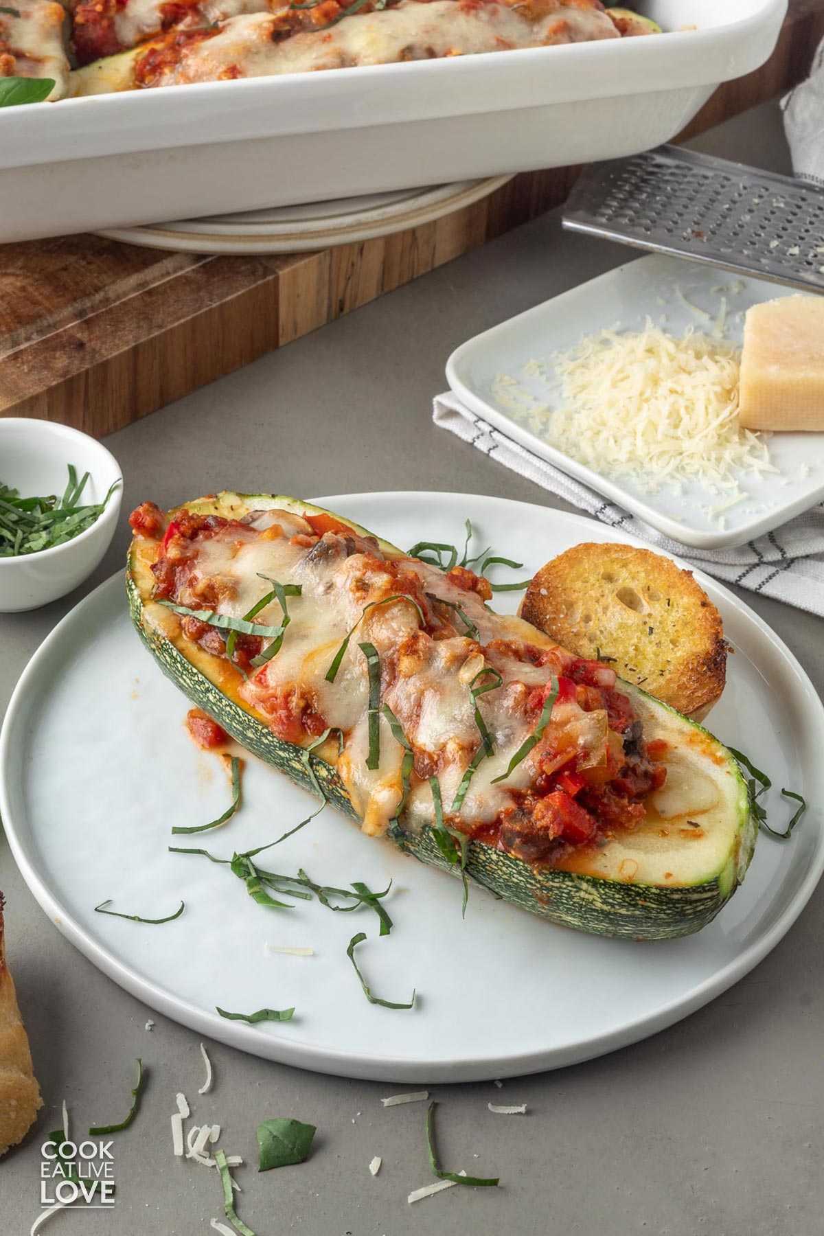 Stuffed vegetarian zucchini served up on a plate with the casserole dish in the back and a plate of parmesan.