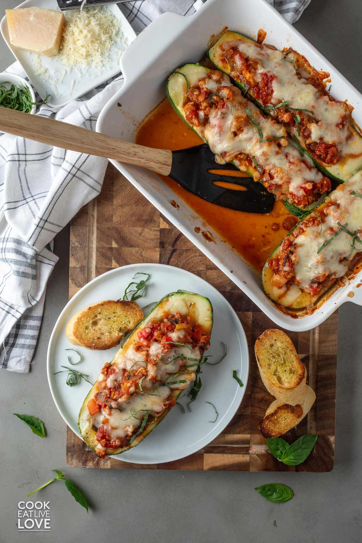 An overhead image of stuffed zucchini boats vegetarian in a casserole dish with a spatula and one served on a plate.