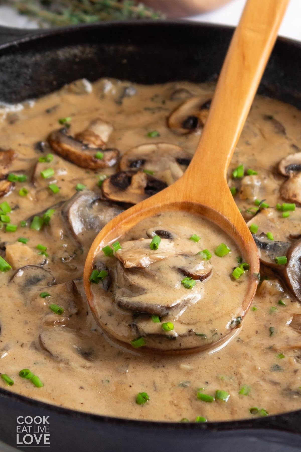 A skillet of vegan mushroom sauce with a wooden spoon resting in the skillet. 