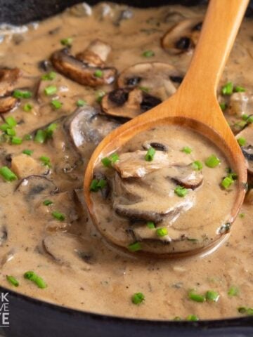 Vegan mushroom sauce in a skillet with a wooden spoon in the skillet.