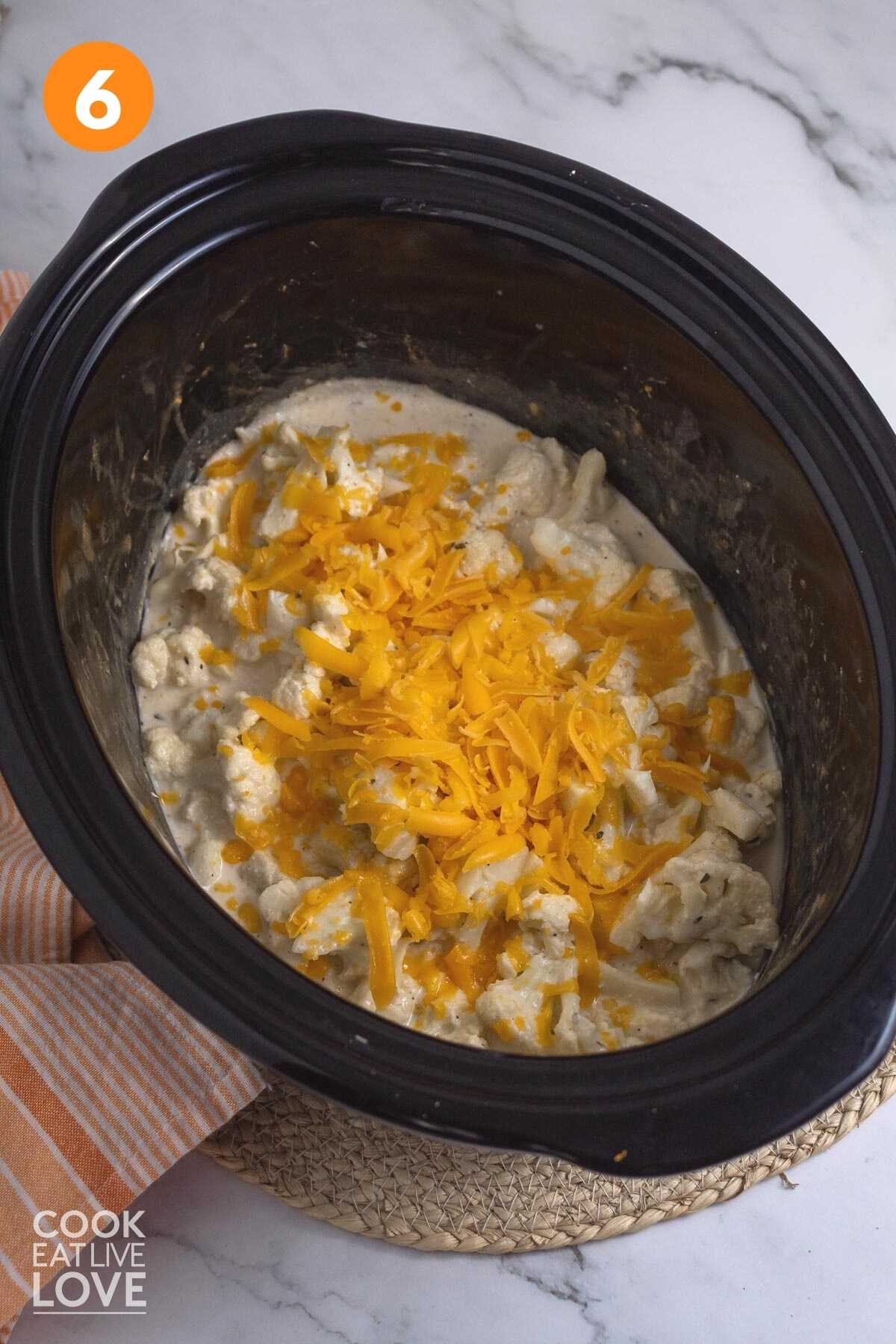 Overhead of cauliflower mixture in a crockpot with the remaining cheddar cheese sprinkled on top.