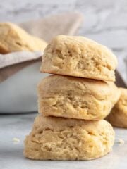 front view of three dairy free biscuits stacked on top of each other on a marble surface. with more biscuits and berries in the background.