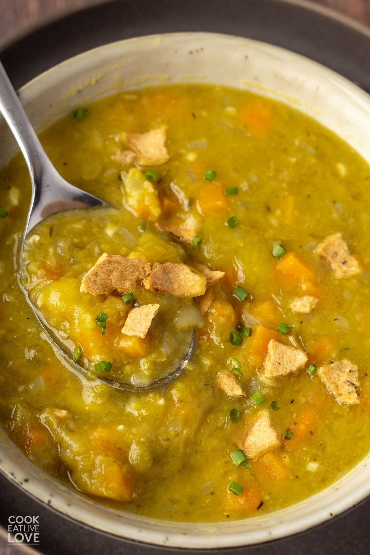close-up of a spoonful of soup above a bowl of soup garnished with crushed cracker pieces.