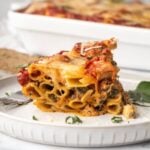 A serving of meatless baked ziti served up on a plate with casserole dish in the background.