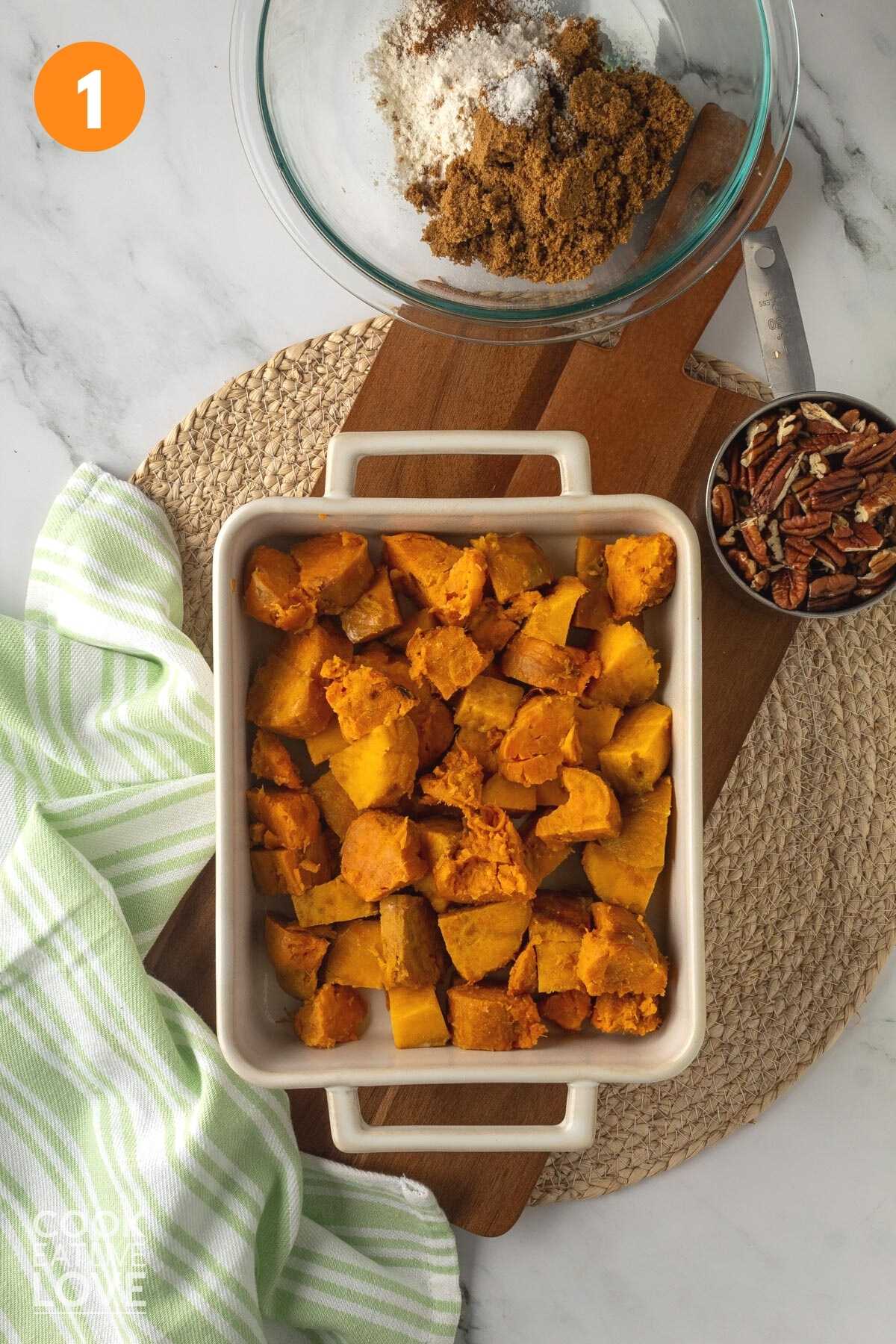 Overhead shot of chopped sweet potatoes in a white casserole dish with other ingredients surrounding it.