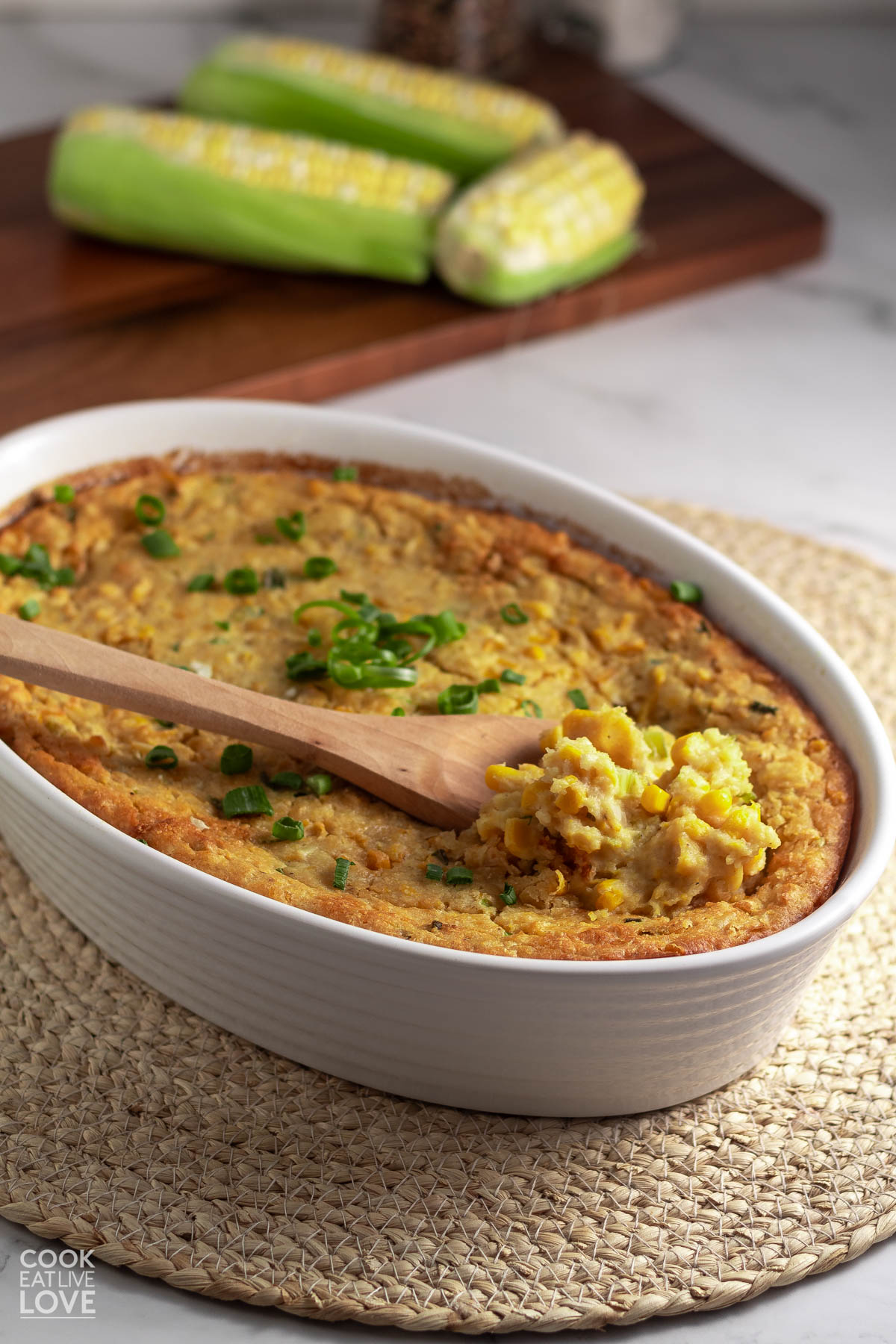 Vegan corn casserole in an oval white baking dish with a wooden spoon in it scooping some out.
