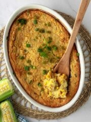 Close-up overhead shot of vegan corn casserole in a white baking dish with a wooden spoon in it scooping some of it out of the dish.