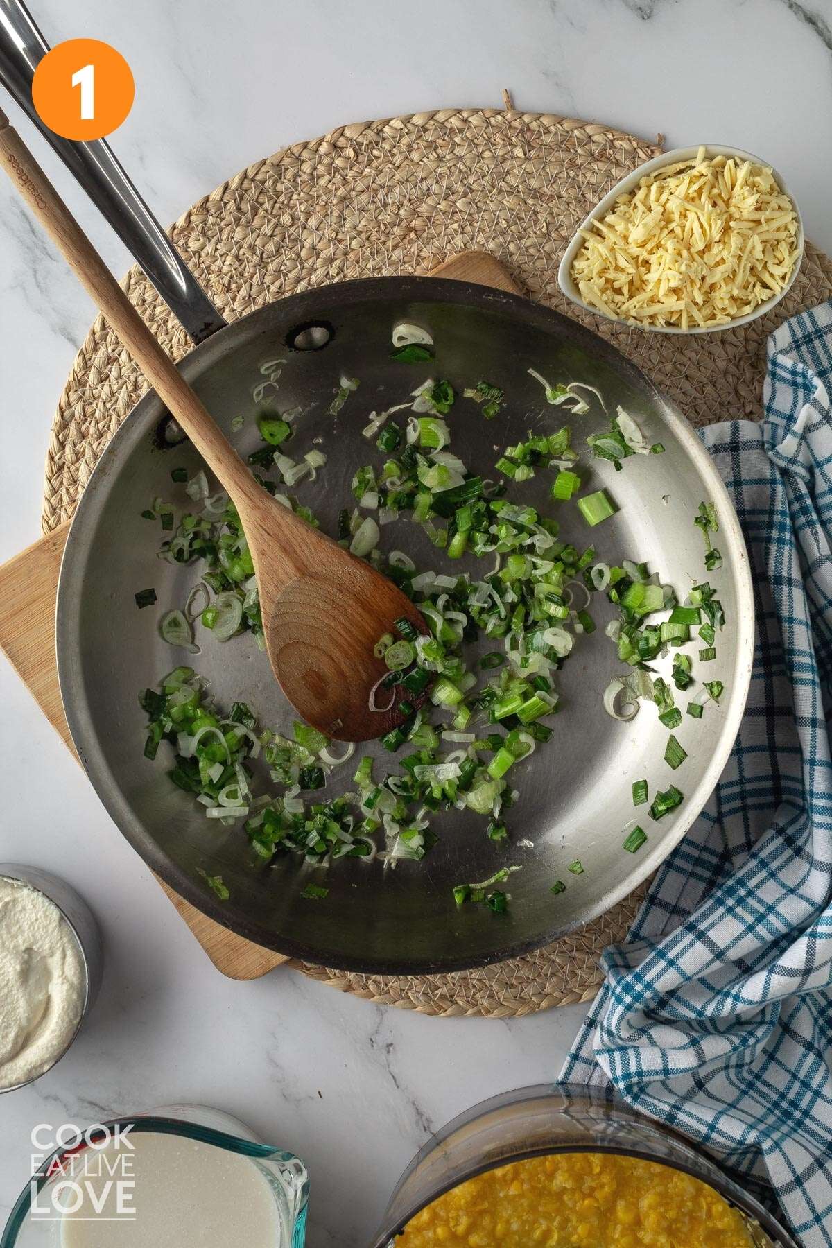 Green onions in a skillet with a wooden spoon in it and other ingredients around it.