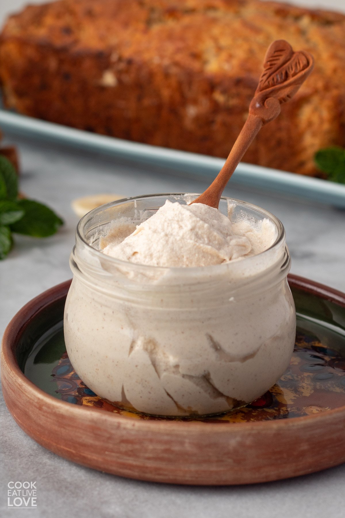 Frosting for banana bread in a glass jar with a wooden spoon in it.