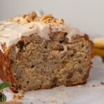 Close-up shot of open loaf of frosted banana bread with self rising flour on a piece of parchment paper.