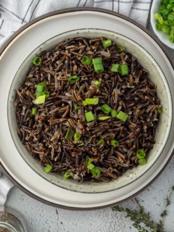 A bowl of instant pot wild rice served up on the table and garnished with green onions.