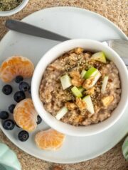 An overhead image of a bowl of slow cooker apple oatmeal on the table with fruit on the plate and a spoon.