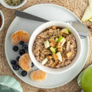 An overhead image of a bowl of slow cooker apple oatmeal on the table with fruit on the plate and a spoon.