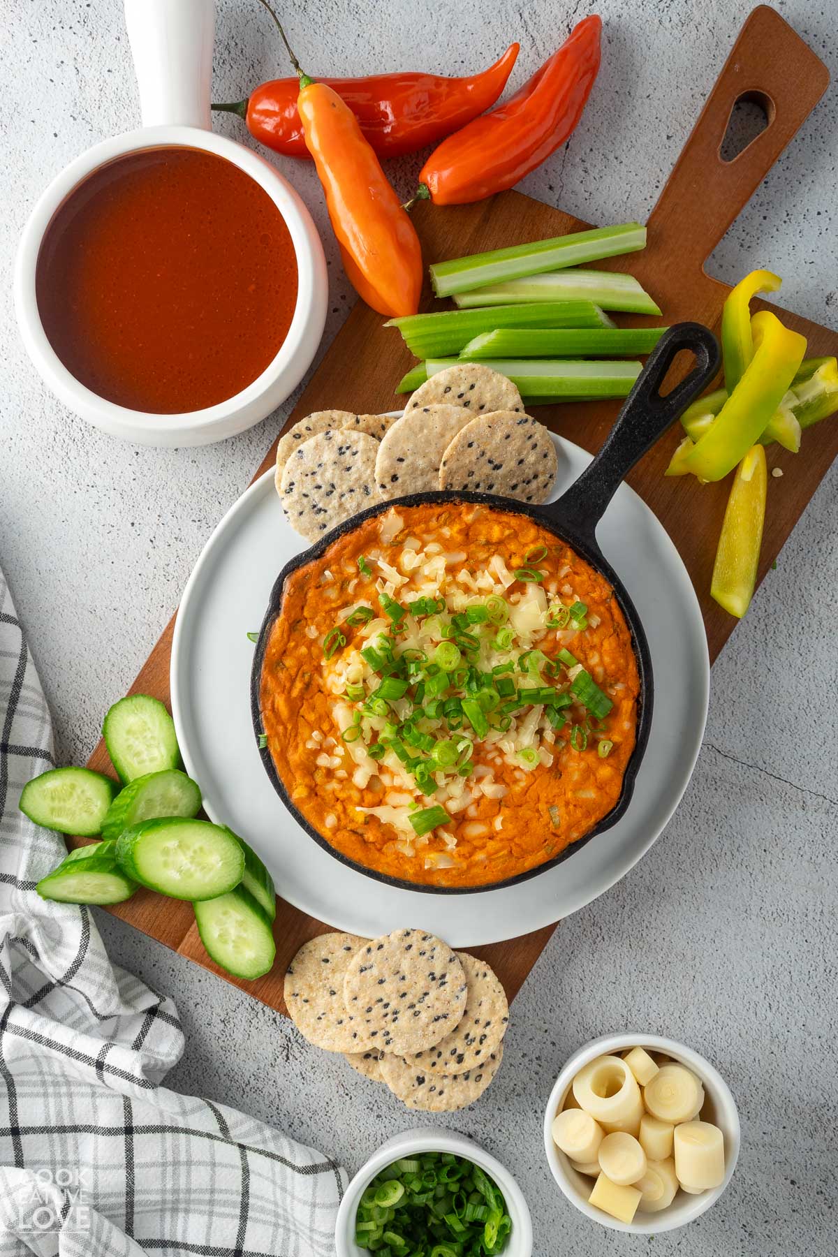 A bowl of vegan buffalo chicken dip on a plate with veggie sticks and crackers on the table.