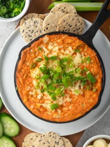 A small skillet of vegan buffalo chicken dip on the table garnished with cheese and green onions.