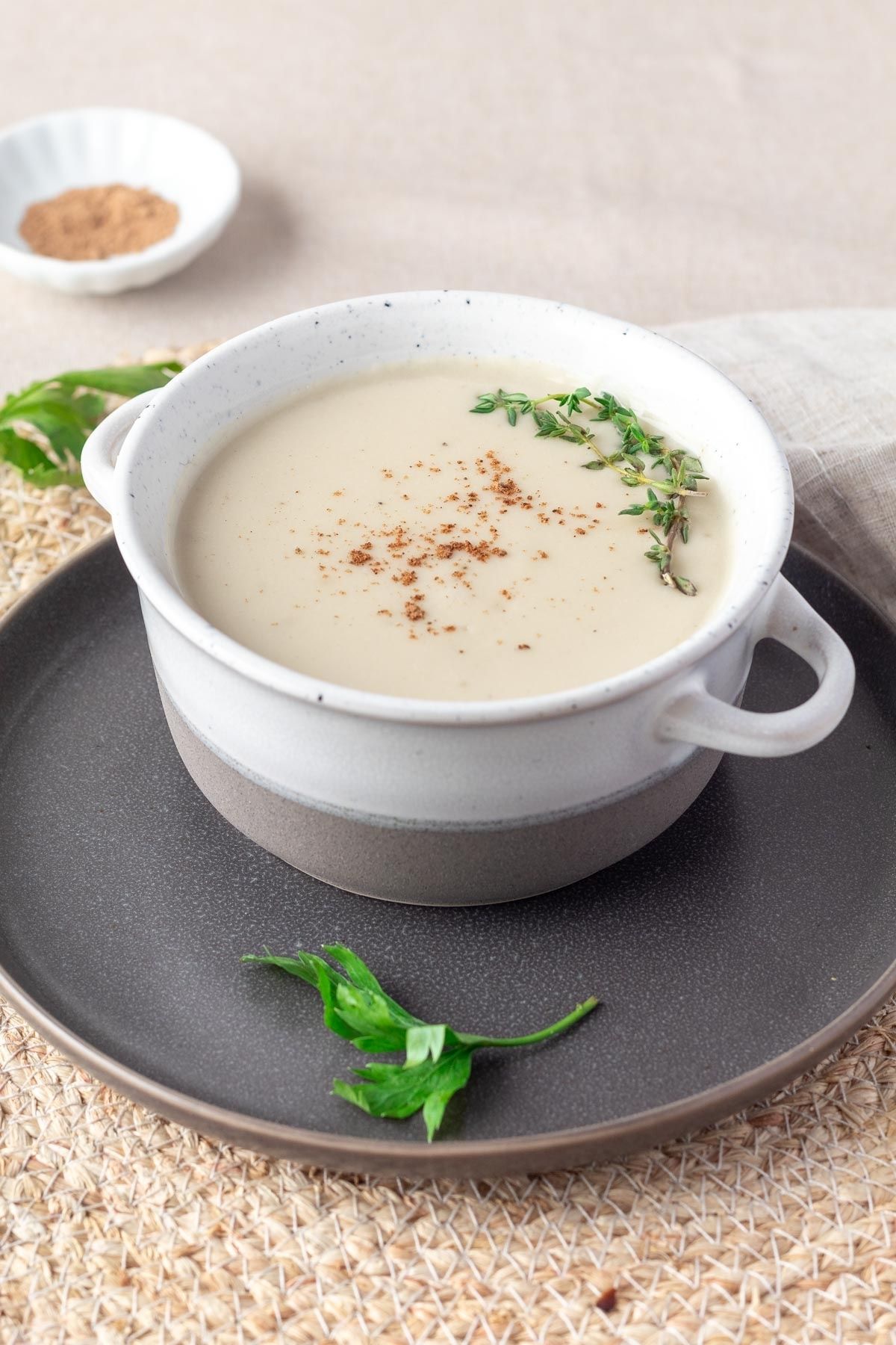 A bowl of vegan bechamel sauce with a sprig of thyme and sprinkle of nutmeg on top.