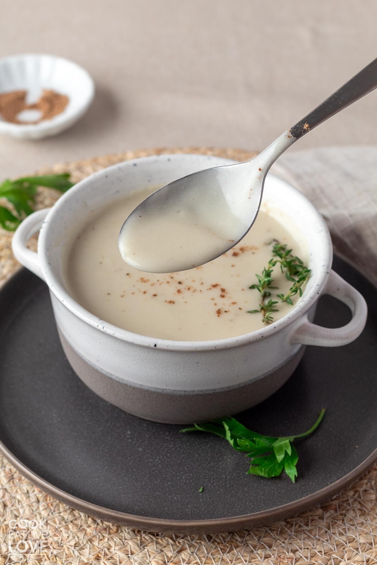A spoonful of vegan white sauce held up over the bowl and the table to show the texture.