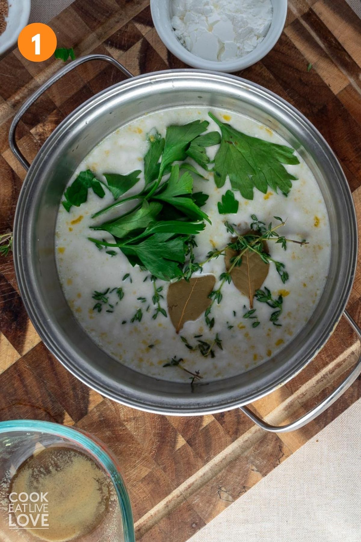 Coconut milk in a saucepan with parsley, thyme, and bay leaves added.