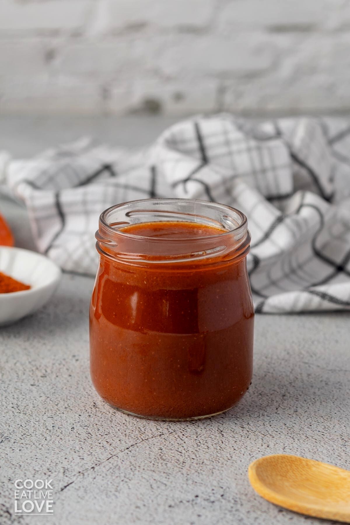 A jar of buffalo sauce made vegan on the table with a towel behind it.