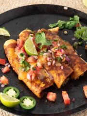 Mushroom enchiladas on a comal garnished with pico de gallo and limes.