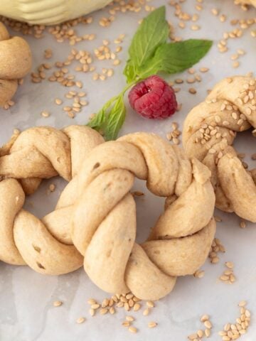 Three rosquitas cookies on a piece of parchment with sesame seeds scattered, fresh mint, and raspberries.