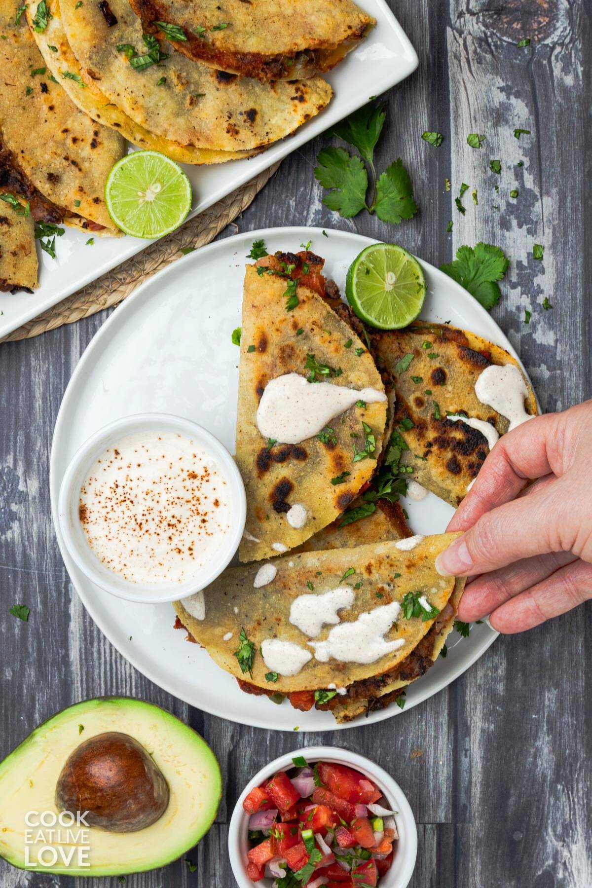 Three crispy black bean tacos on a white plate with a chipotle yogurt dip and limes.