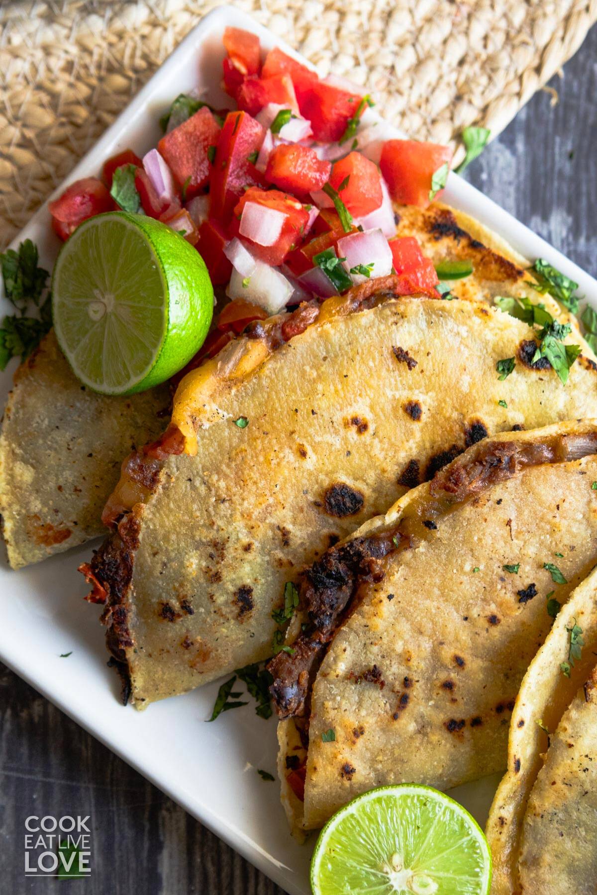 Crispy black bean tacos on a white platter with a lime and some pico de gallo.