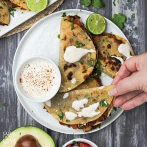 A hand reaching in to grab a crispy black bean taco from a plate.