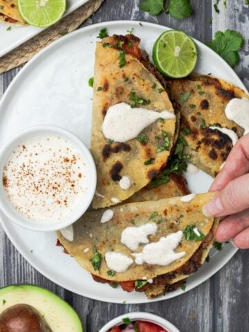 A hand reaching in to grab a crispy black bean taco from a plate.