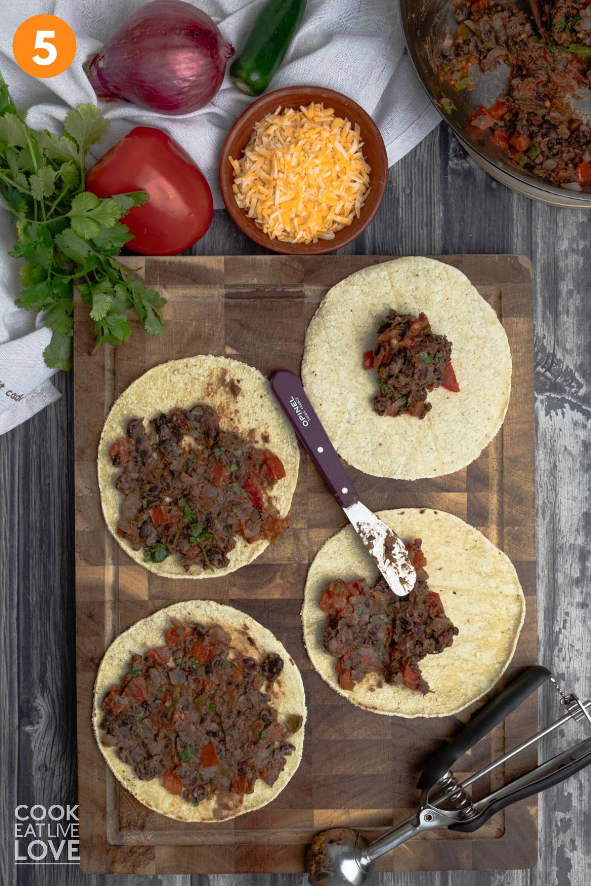 Black beans spread on top of corn tortillas laid out on a wooden cutting board.