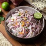 Peruvian salsa criolla in a bowl on a dark wood cutting board with whole ingredients around it.